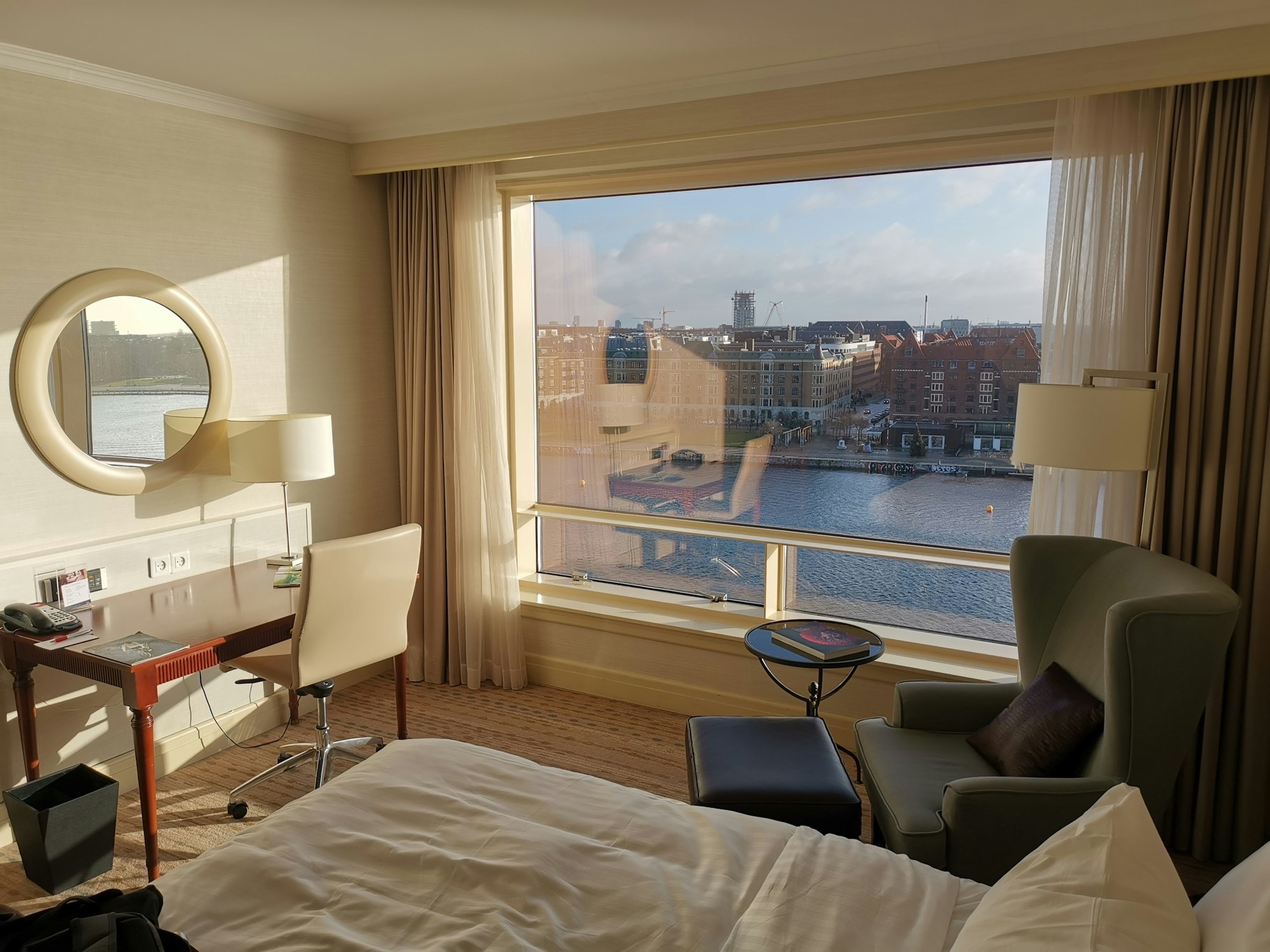 A hotel room with a wide window over a city harbor